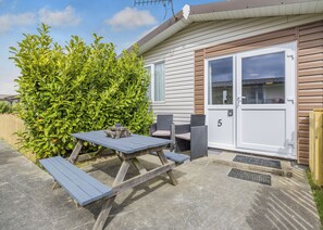 Une maison mobile dotée d’un patio comprenant une table de pique-nique et des chaises, un petit jardin et le numéro « 5 » sur la porte.