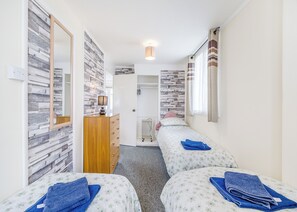 Une chambre avec deux lits, une commode, un miroir, un radiateur et une fenêtre avec des rideaux.