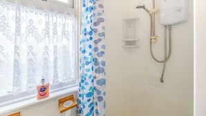 Un baño con ducha, una ventana con cortinas de encaje y una botella de jabón Carex.