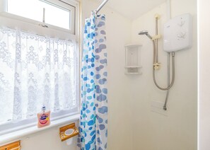 Une salle de bain avec une douche, une fenêtre orn ée de rideaux en dentelle et un flacon de savon Carex.
