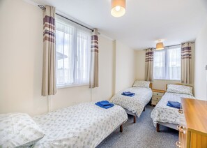Ein Zimmer mit zwei Einzelbetten, einem Holztisch und einem Fenster mit Vorhängen.