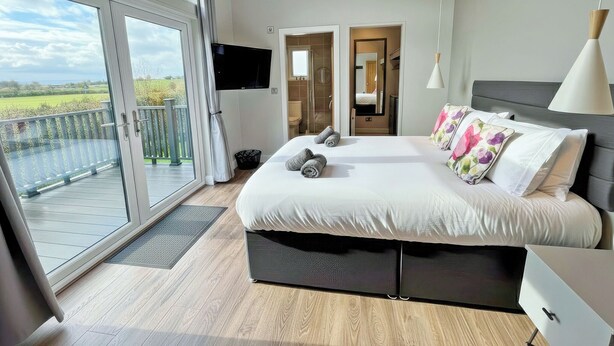 A bedroom with a large bed, a TV, a desk, and a balcony with a view.