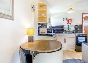 Una cocina compacta con una mesa de comedor, sillas, microondas, estufa y un reloj en la pared.