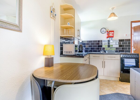 Una cocina compacta con una mesa de comedor, sillas, microondas, estufa y un reloj en la pared.