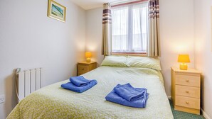 Een slaapkamer met een bed, twee nachtkastjes, een raam met gordijnen, een radiator en een schilderij aan de muur.