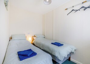 Una habitación pequeña y limpia, con dos camas individuales, una mesita de noche con lámpara y un perchero con perchas.