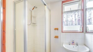 Een badkamer met een douche met glazen wanden, een witte wastafel en een raam met uitzicht op gebouwen.
