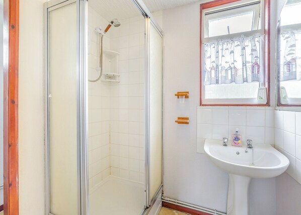 Un baño con ducha de vidrio, un lavamanos blanco y una ventana con vista a edificios.