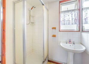 A bathroom with a glass-enclosed shower, a white sink, and a window with a view of buildings.