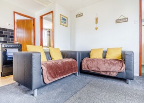 A living room with a sofa, a kitchen area, and a door leading to another room.