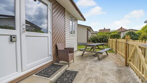 Ein Wohnhaus mit Garagentor, einer Terrasse, einem Picknicktisch und Stühlen sowie einem Holzzaun.