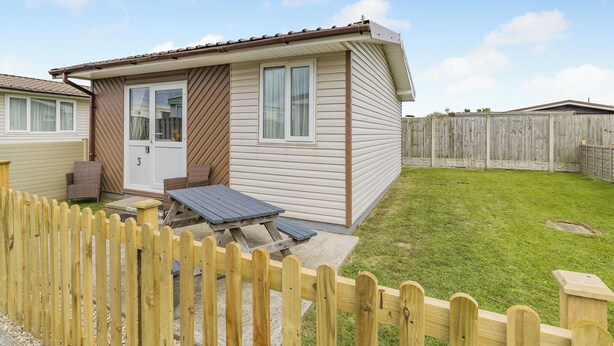 Een gelijkvloerse stacaravan met een terras, een omheind gazon en een houten terras.