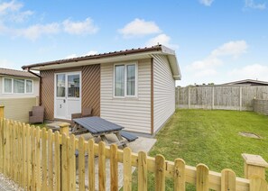 A single-story mobile home with a patio, a fenced yard, and a wooden deck.