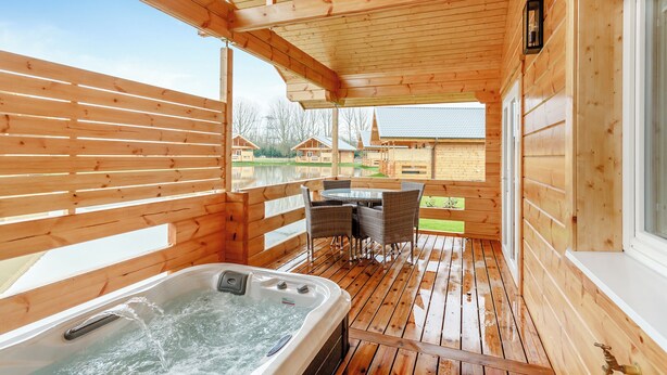A wooden deck with a hot tub, outdoor seating, and a view of cabins.
