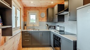 A compact kitchen with wooden walls, a sink, a microwave, a toaster, and a refrigerator.