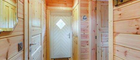 A wooden hallway with doors, a white door with a diamond pattern, and a small circular sign on the wall.