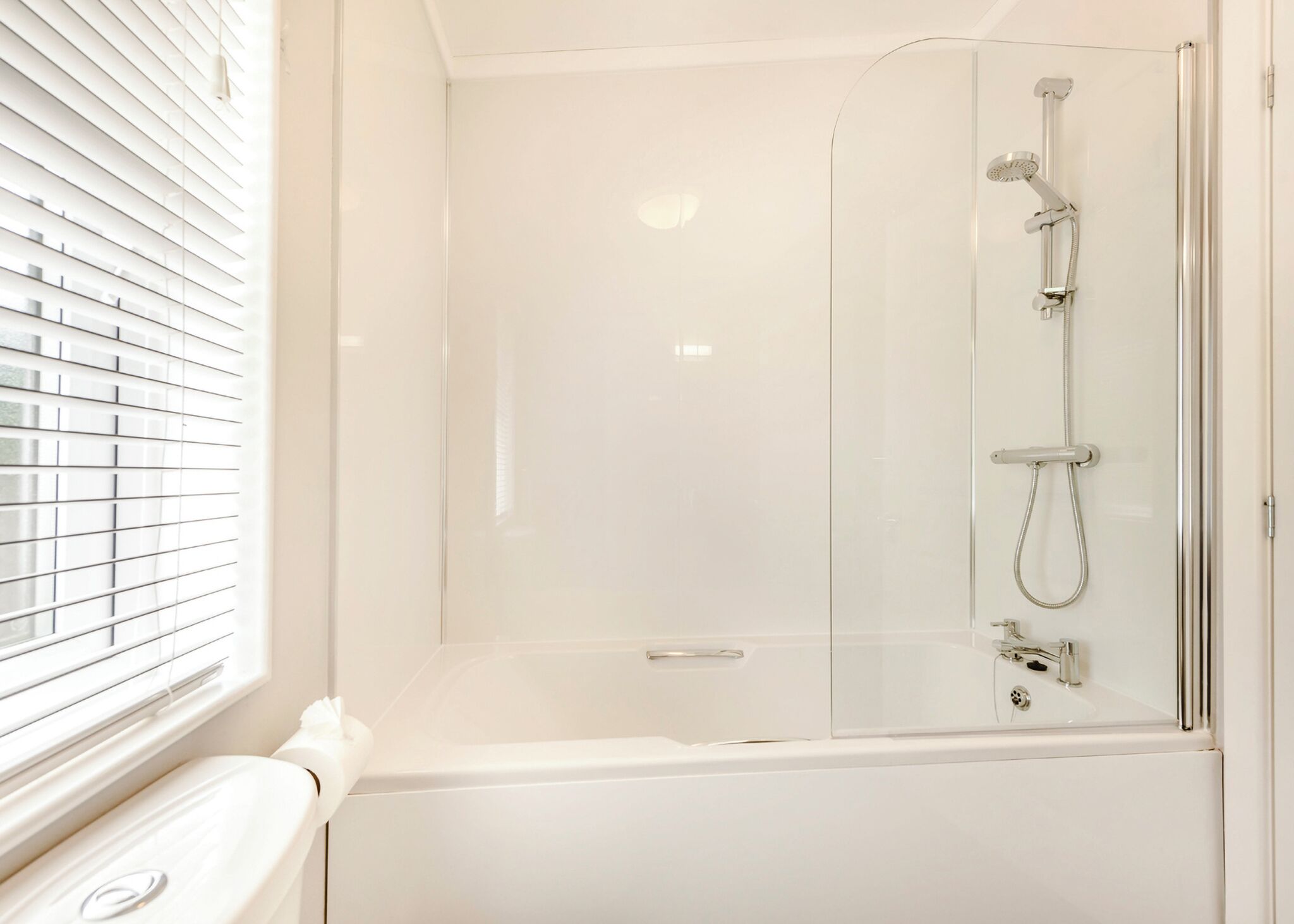 Un baño moderno con ducha acristalada, bañera blanca y ventana con persianas.