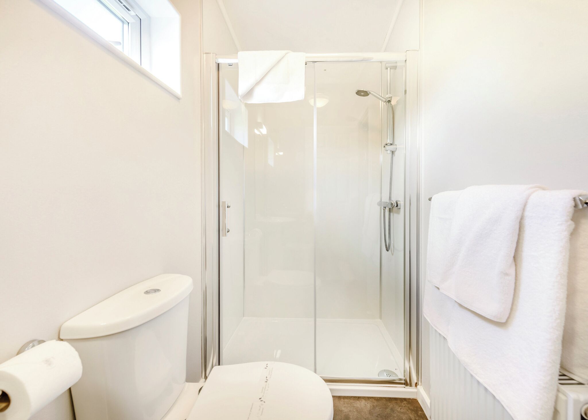 A small, modern bathroom with a glass-enclosed shower, a toilet, and a towel rack.