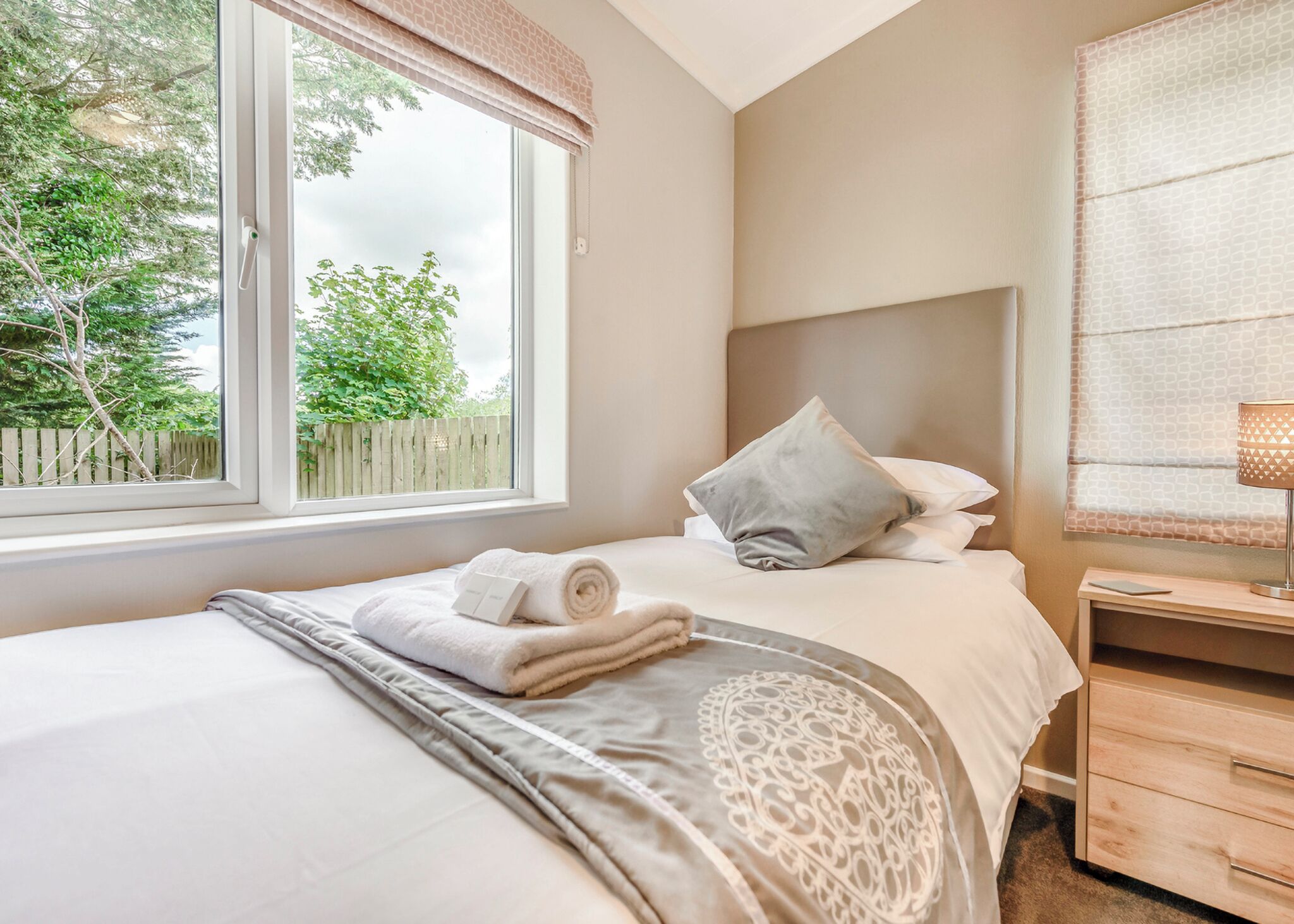 A bedroom with a bed, a nightstand, a lamp, and a window with a view of trees.