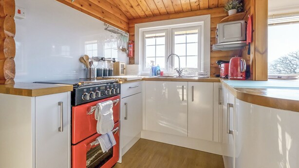 Una cocina con techo de madera, armarios blancos, un horno rojo y una ventana con vistas.