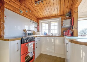 Una cocina con techo de madera, armarios blancos, un horno rojo y una ventana con vistas.