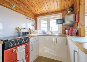 A kitchen with a red stove, white cabinets, a wooden ceiling, and a window.