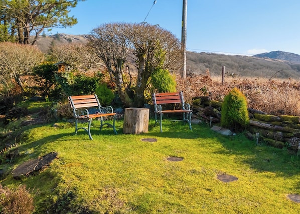 A garden with two wooden benches, a tree, and a stone wall.