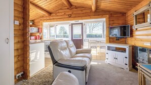 Interior de una cabaña de madera con sofá, televisión y zona de cocina.