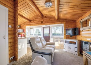 L’intérieur d’une cabane en rondins, avec un canapé, un téléviseur et un coin cuisine.