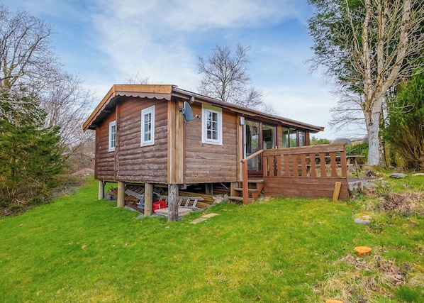 A wooden cabin with a porch, a satellite dish, and a small deck.