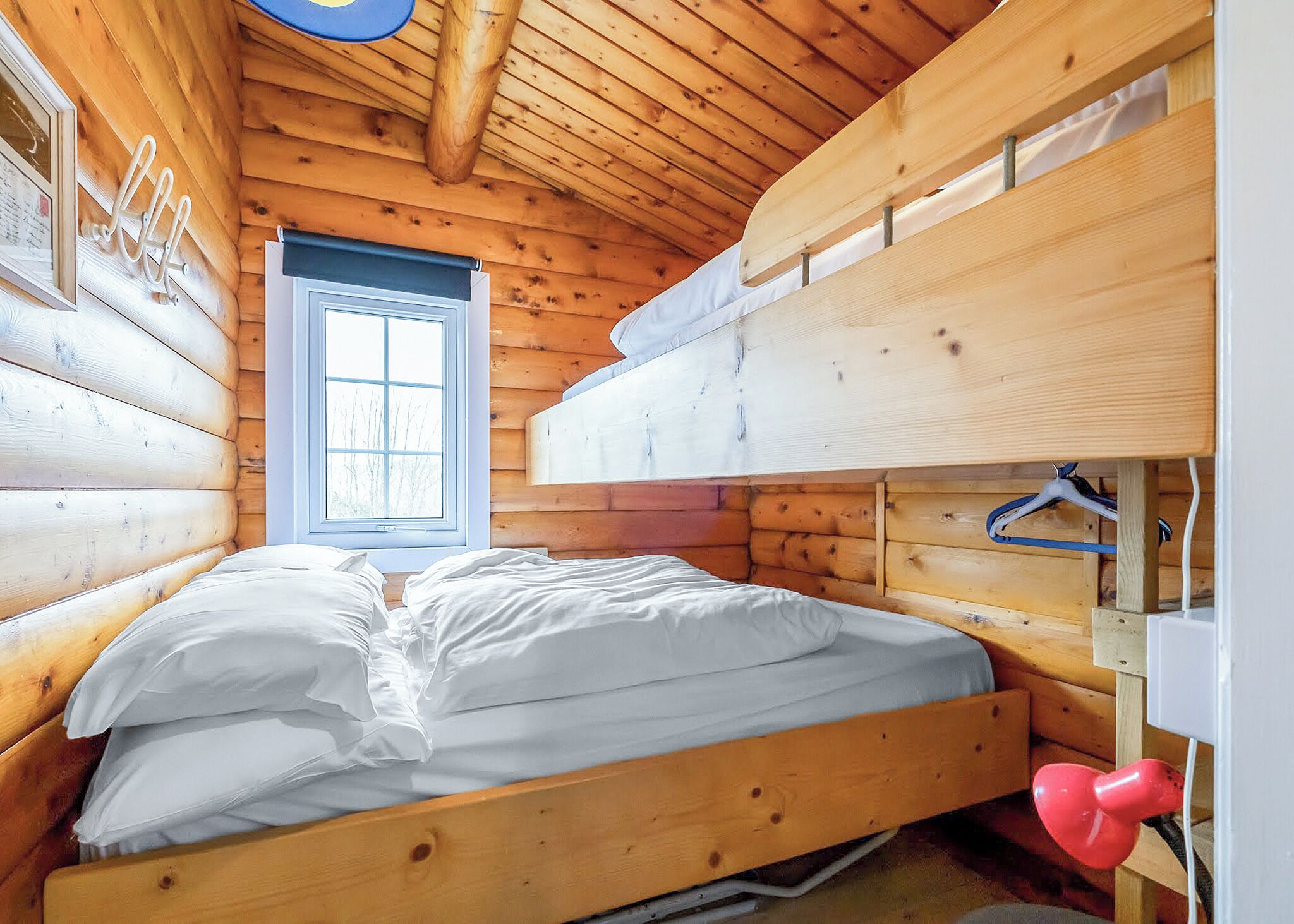 Ein Zimmer in einer Holzhütte mit einem Etagenbett, einem Fenster und einem Bett mit weißer Bettwäsche.