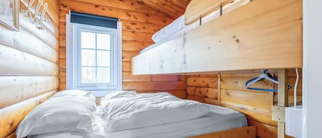 Quarto de cabana de madeira com beliche, janela e cama com roupa de cama branca.
