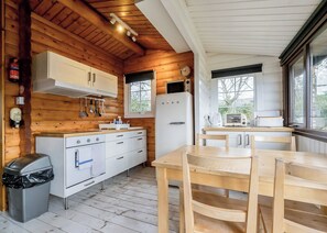 A compact kitchen with wooden walls, a white refrigerator, a stove, and a dining area with a table and chairs.