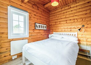 Ein Schlafzimmer in einer Holzhütte mit einem Bett, einem Fenster, einem gerahmten Foto und einer Lampe.