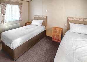 Une chambre avec deux lits, une fenêtre avec des rideaux, un radiateur et une table de chevet en bois.