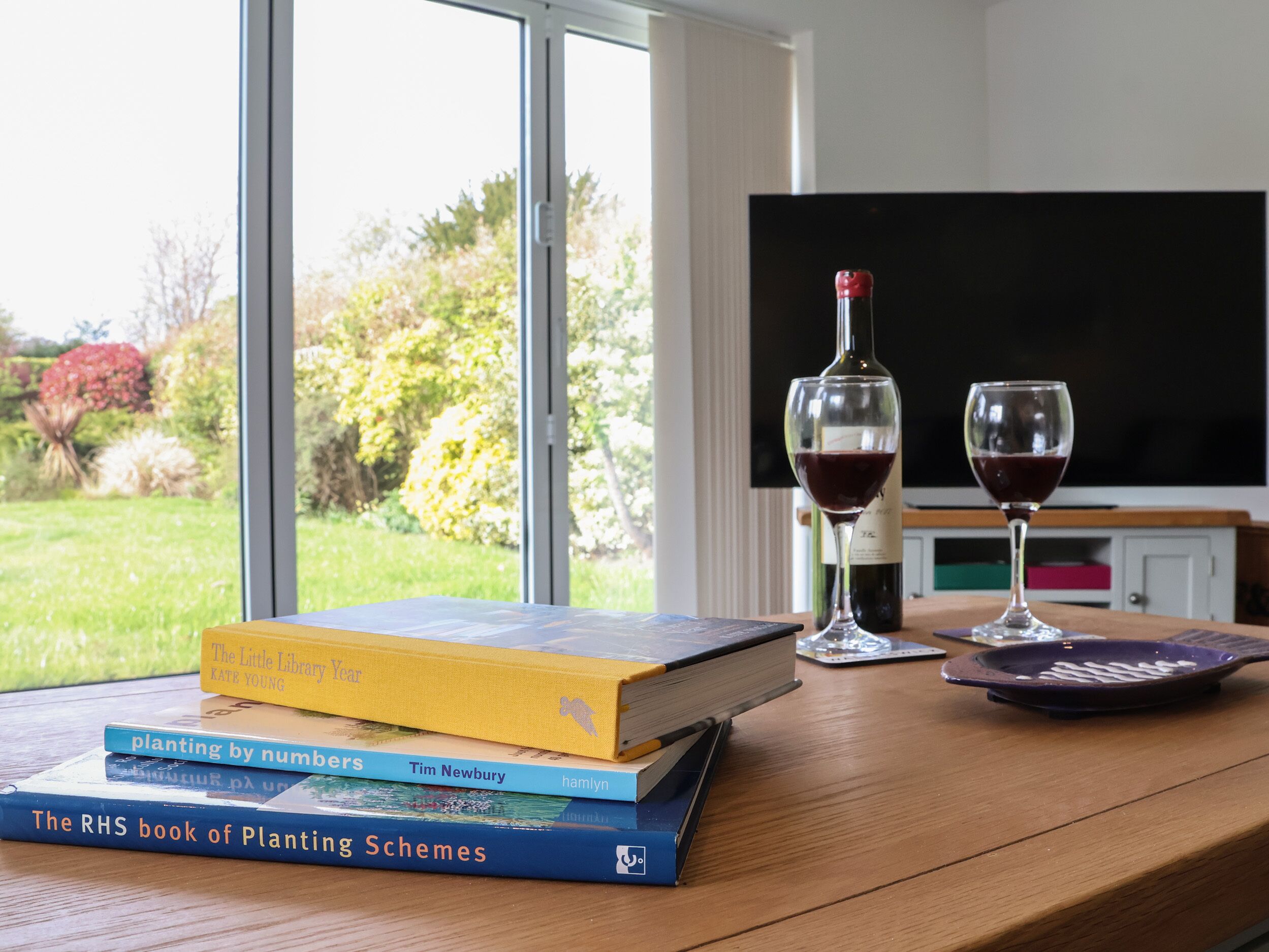 Ein Holztisch mit einer Stapel Bücher, zwei Weingläsern und einer Weinflasche.