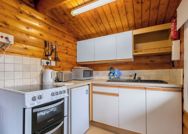 A compact kitchen with white cabinets, a microwave, a toaster, a kettle, and a dishwasher.