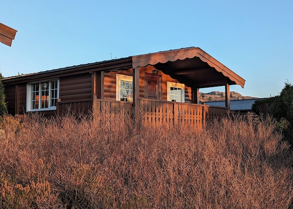 Eine Holzhütte mit Veranda, Fenstern und Blick auf eine Berglandschaft.