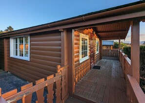 A wooden cabin with a porch, large windows, and a view of the surrounding landscape.