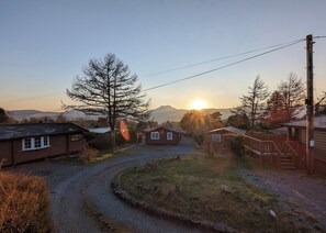 A rural cabin area with a gravel path, wooden cabins, and a mountain backdrop.