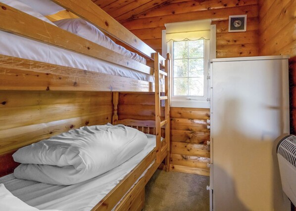 Eine Hütte mit Etagenbetten, einem Kühlschrank und einem Fenster mit Blick auf Bäume.