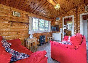 Ein Blockhaus-Interieur mit einem roten Sofa, einem Fernseher und einem Kamin.
