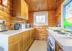 Eine kleine Küche mit Holzwänden, einem Fenster und einfachen Geräten wie Toaster, Wasserkocher und Mikrowelle.