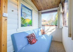 Ein Zimmer mit einem blauen Sofa, einem Buntglasfenster und Blick auf eine Holzterrasse.