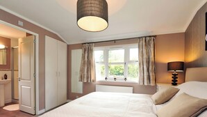 Een slaapkamer met een groot bed, een nachtkastje met een lamp, een raam met gordijnen, een radiator en een kledingkast.