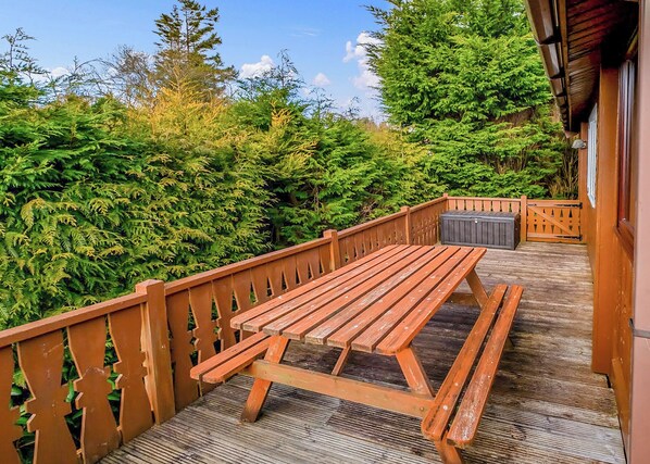 A wooden deck with a picnic table, surrounded by dense greenery and trees.