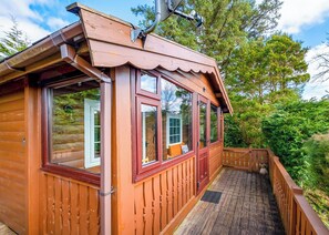 A wooden cabin with large windows, a porch, and a view of the surrounding forest.