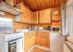 A compact kitchen with wooden cabinets, a stove, a microwave, and a sink.
