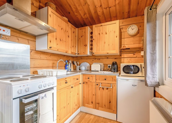 A compact kitchen with wooden cabinets, a stove, a microwave, and a sink. - 2 bedroom accommodation in Blaenau Ffestiniog (Blaenau Ffestiniog)