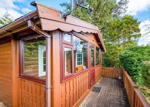 A wooden cabin with large windows, a porch, and a view of the surrounding forest.